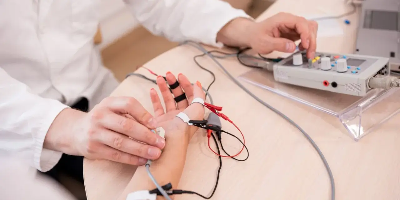 Lekarz wykonuje próbę tężyczkową, podłączając elektrody do dłoni pacjenta i regulując aparat.
