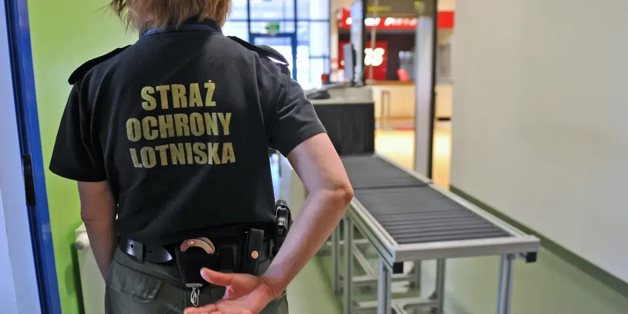 Ochroniarz lotniskowy przy taśmie bagażowej. Zastanawiasz się, czy można przewozić wódkę w bagażu rejestrowanym? Sprawdź przepisy!