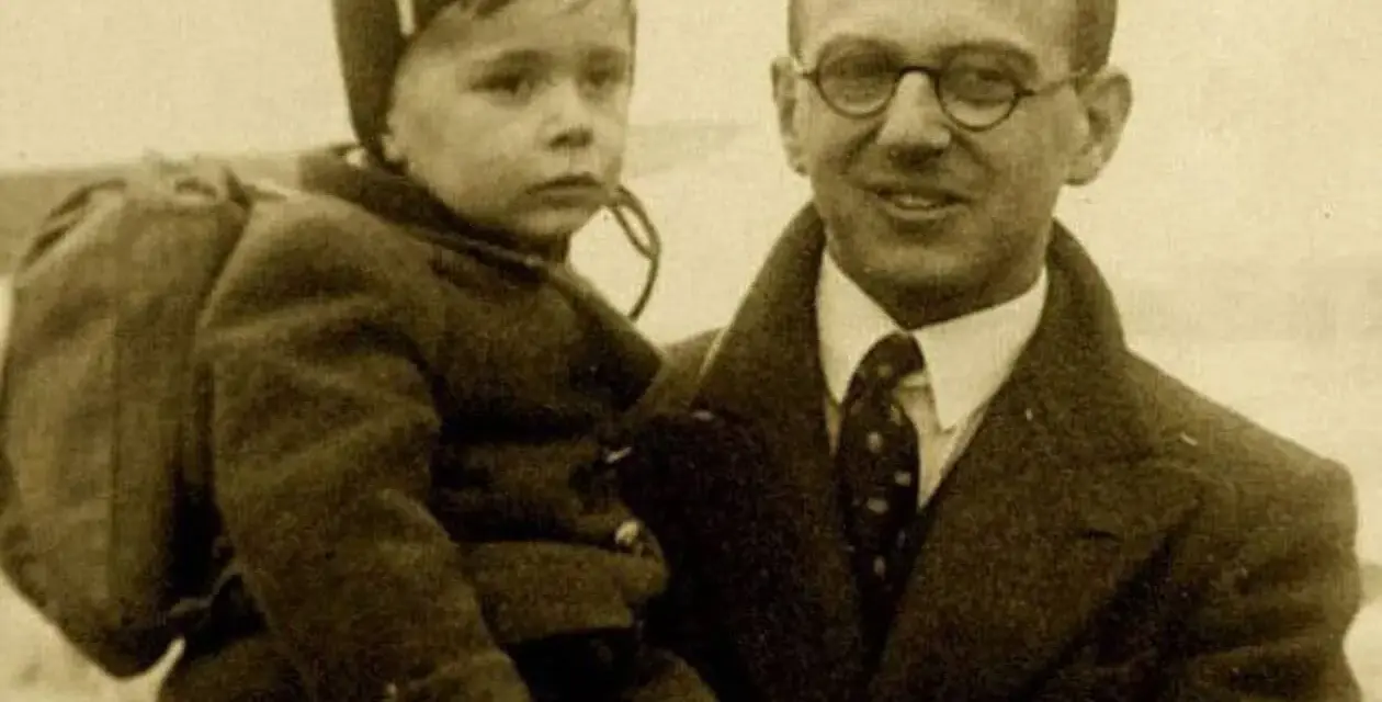 Nick Winton porte un enfant sur son bras, un petit garçon avec un sac à dos, prêt pour un nouveau départ.