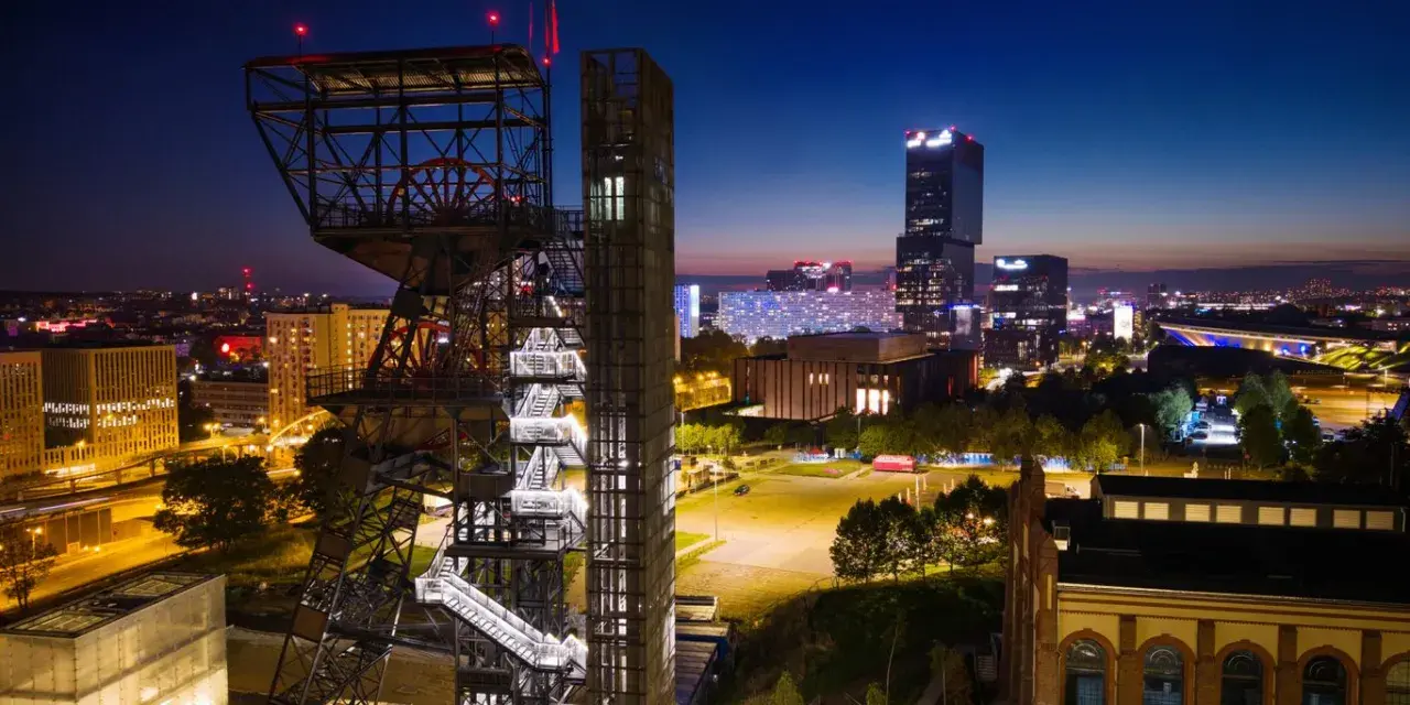 Wieżowiec kopalni węgla obok nowoczesnych budynków tworzy kontrast w nocnym megapolis.
