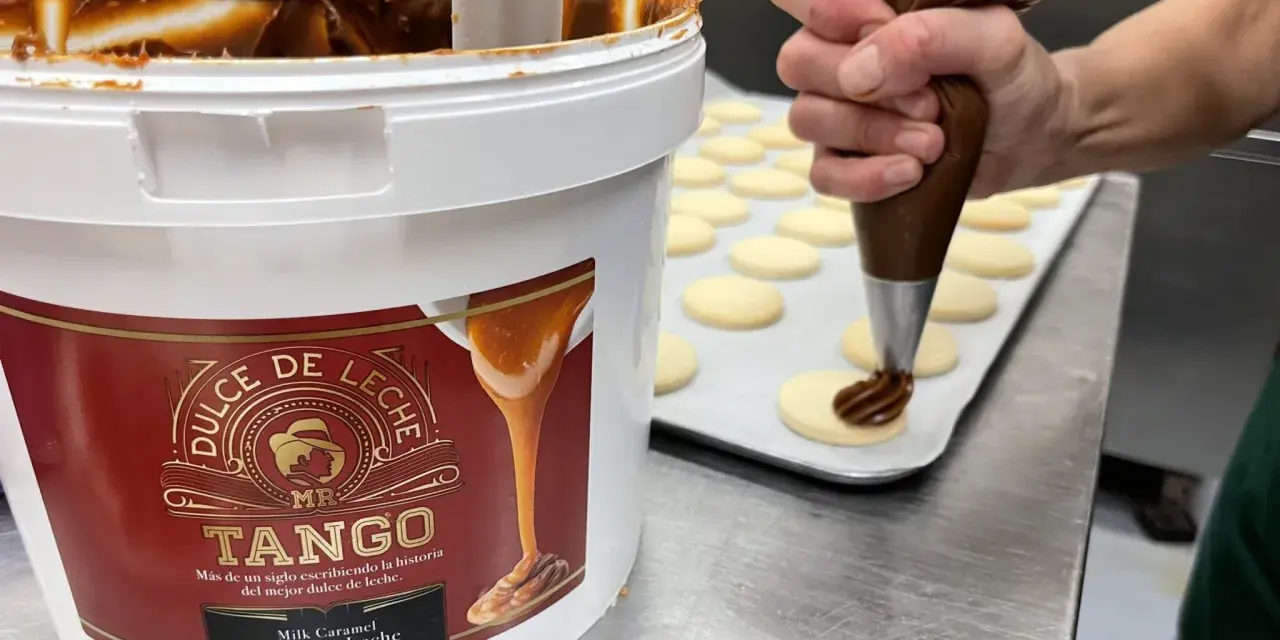 Un repostero decora galletas con una manga pastelera, usando el delicioso dulce de leche de un gran envase.