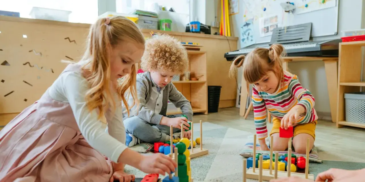 Drei Kinder, darunter ein **kind 8 jahre**, spielen konzentriert mit bunten Holzbausteinen im Kindergarten.