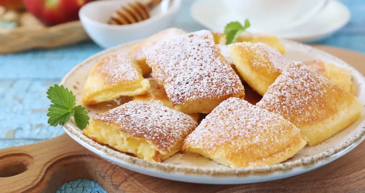 Puszysty omlet z jabłkiem, posypany cukrem pudrem, na talerzu z listkiem mięty. Obok jabłka i miód.