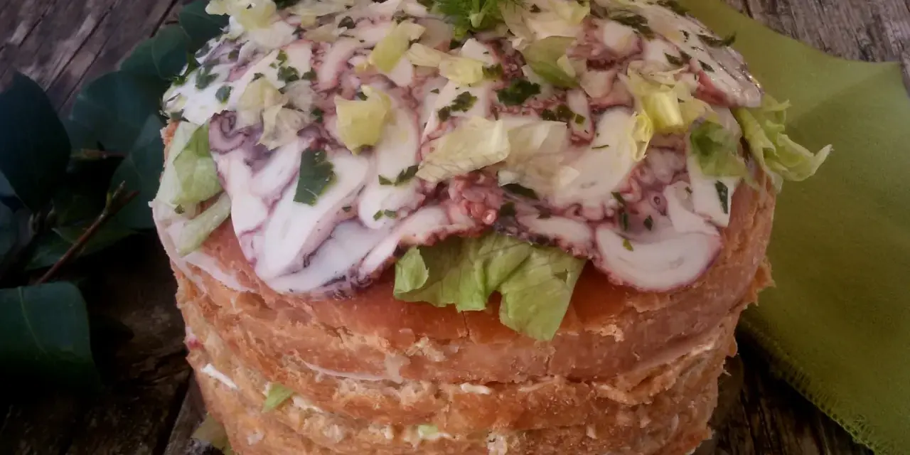 Panettone Gastronomico with sliced octopus, lettuce, and herbs on a wooden table.