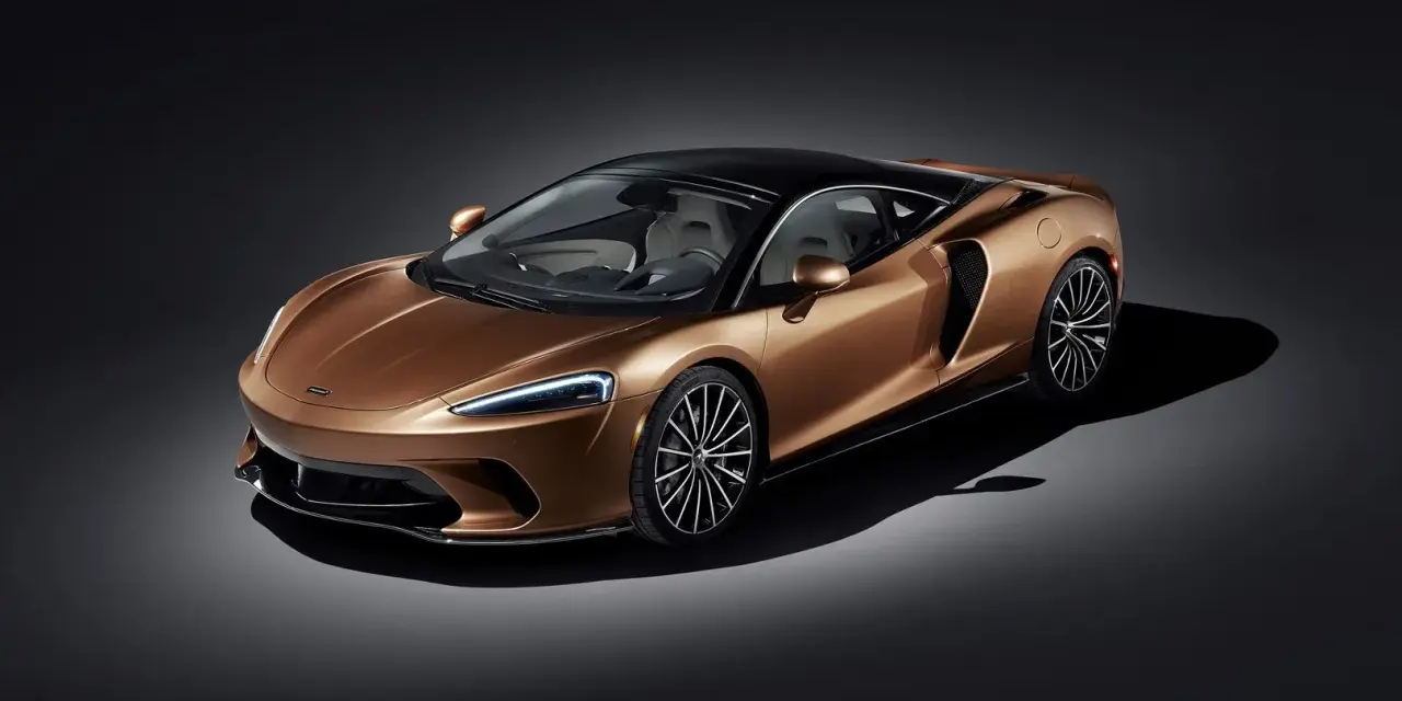 Elegancki, miedziany McLaren GT z czarnym dachem i felgami, prezentujący swoje sportowe linie na ciemnym tle.