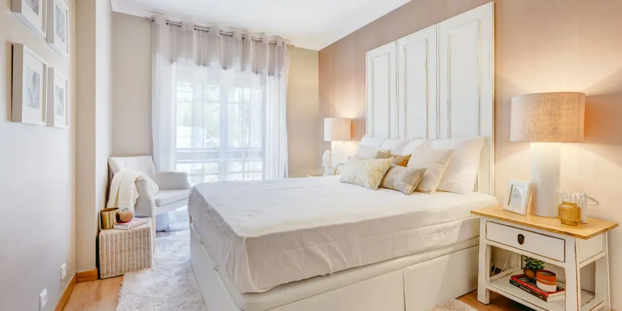 Camera da letto accogliente con letto bianco, comodino con libri e lampada. Idee su cosa mettere su como camera da letto.