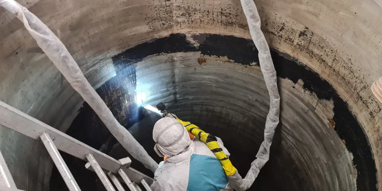 Pracownik w kombinezonie ochronnym wykonuje czyszczenie suchym lodem wnętrza betonowego zbiornika.