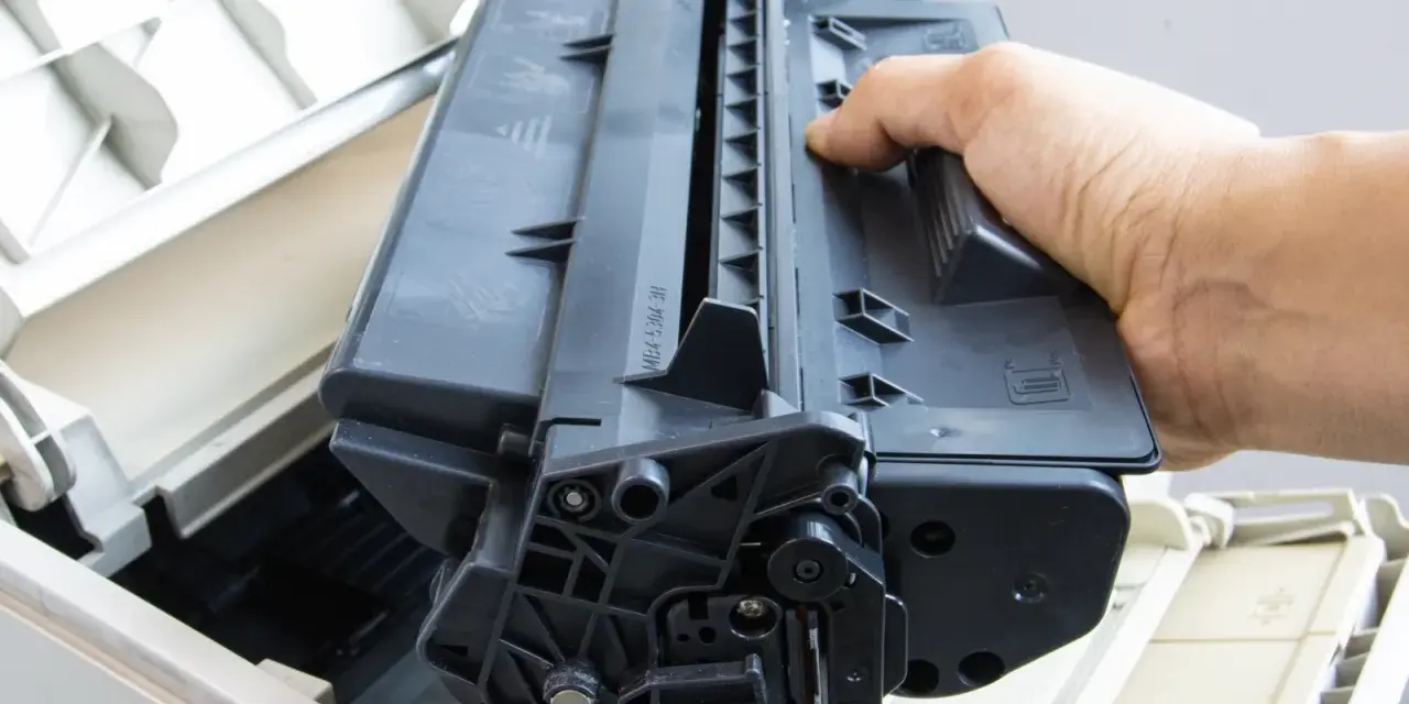 Ręka wyjmuje czarny toner z drukarki. Skorzystaj z naszej oferty bezpłatny odbiór tonerów.