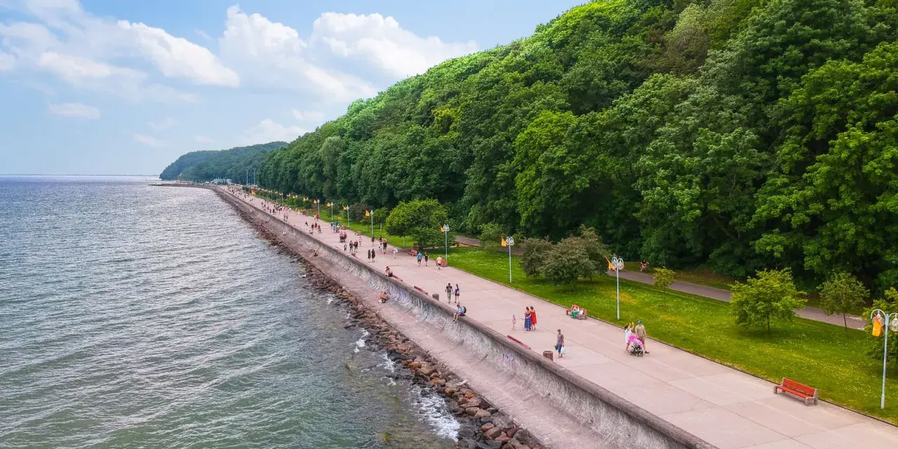 Spacer po molo południowym wzdłuż zielonego wybrzeża. Ludzie spacerują, odpoczywają na ławkach, ciesząc się pięknym dniem nad morzem.