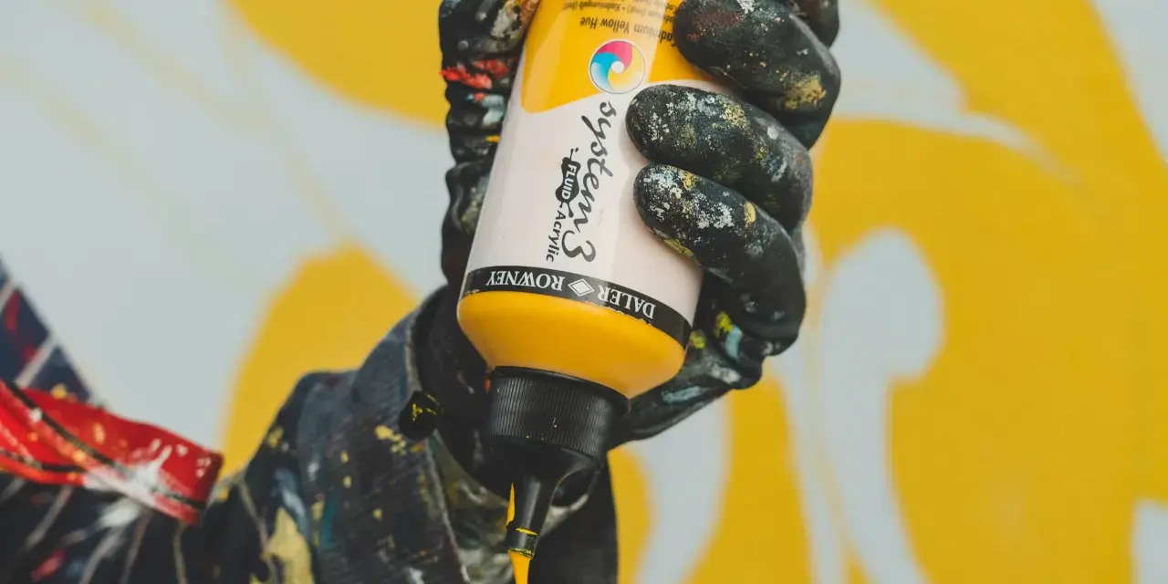 Main jaune de peinture acrylique Daler Rowney System 3, versée par une main gantée, pour un mélange de couleurs.