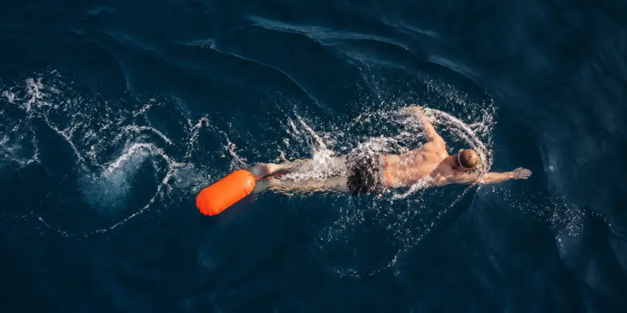 Un nageur profite d'une séance de nage en eau libre, suivi d'une bouée orange vif.