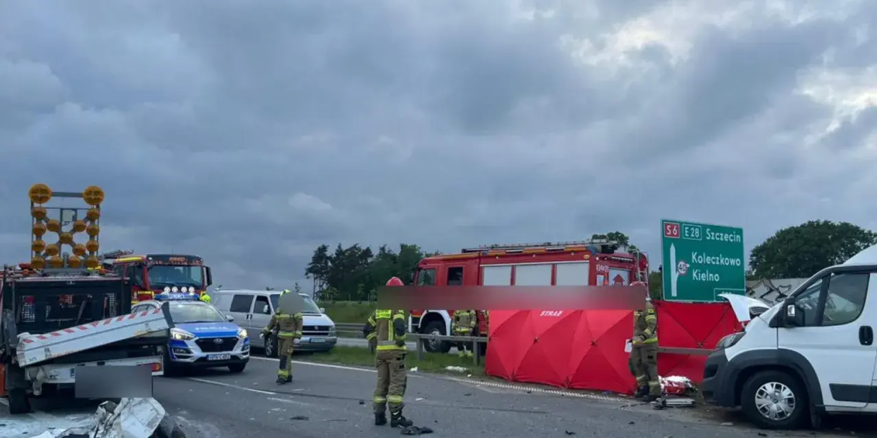 Miejsce wypadku kampera. Straż pożarna i policja zabezpieczają teren po zdarzeniu drogowym. Widoczny rozbity pojazd i czerwony namiot.