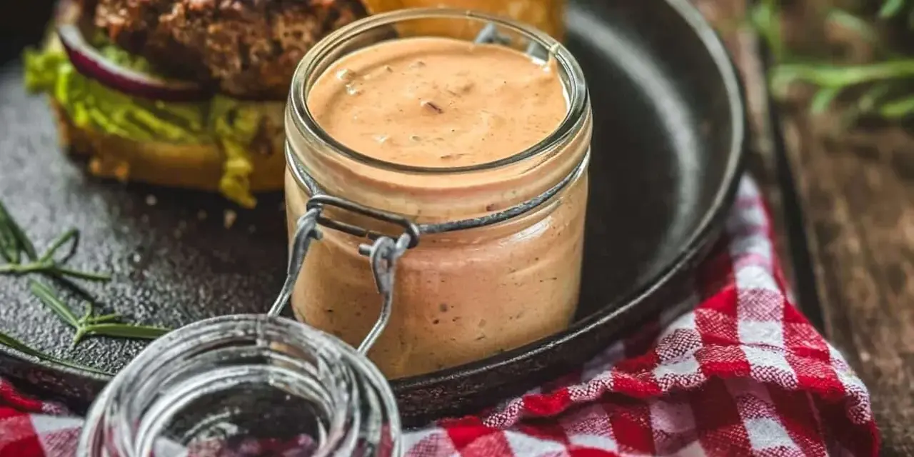 Ein Glas mit selbstgemachter Burgersauce steht neben einem Burger. Perfekt zum burgersauce selber machen!