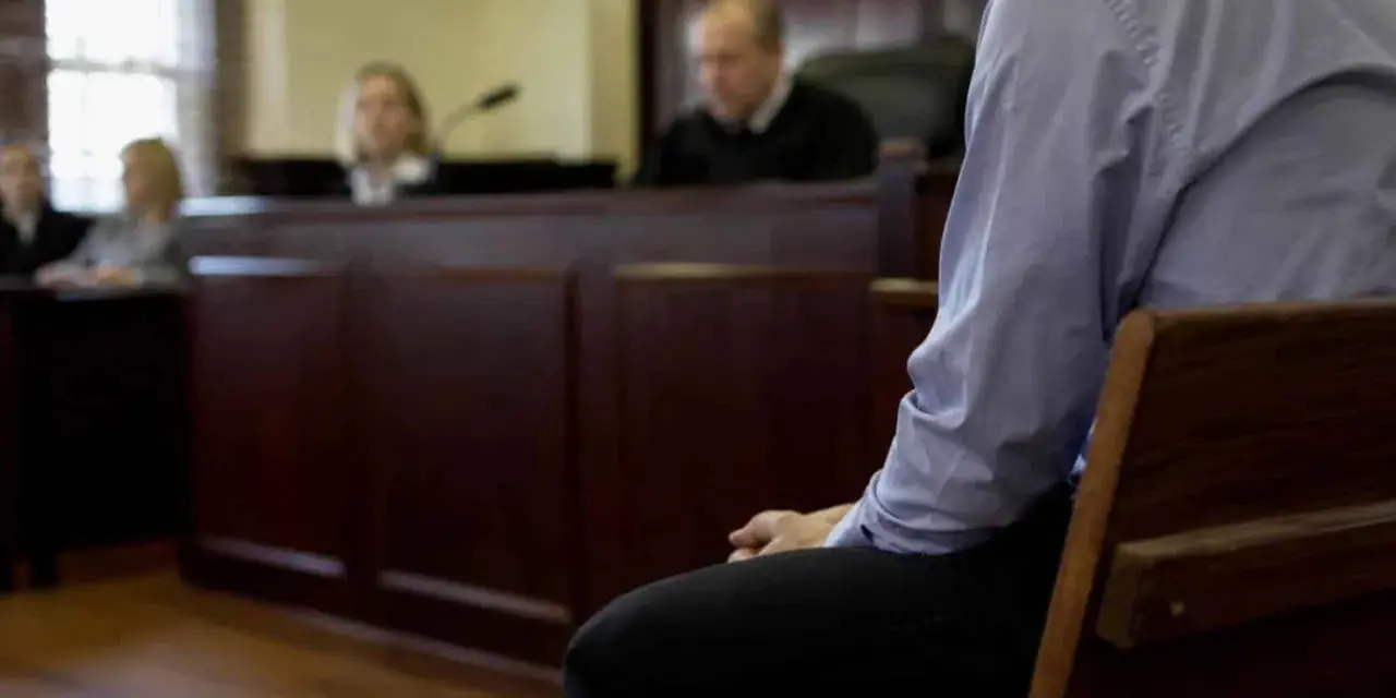 W sali sądowej mężczyzna czeka na werdykt. Czy kara grzywny jest wyrokiem? Sędziowie i ławnicy w tle.