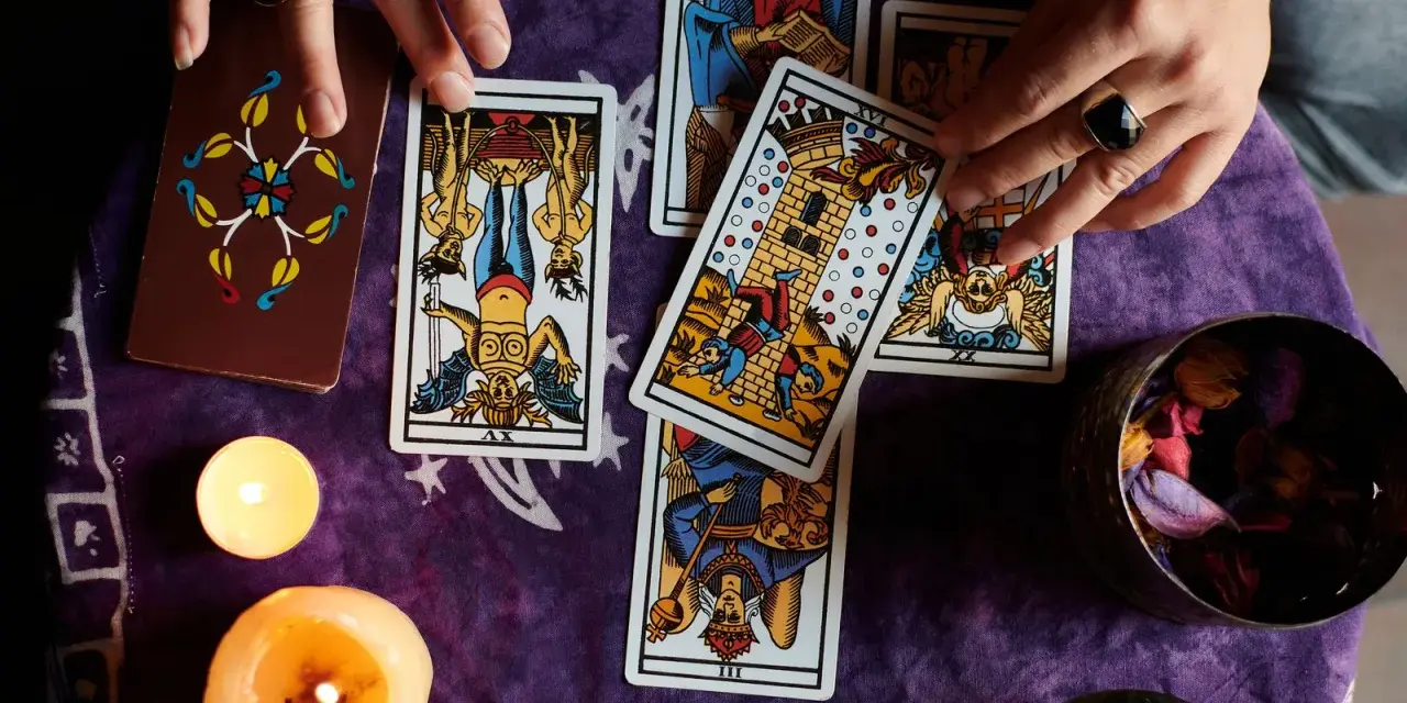 Manos de tarotista que es, barajando cartas y velas encendidas sobre tela morada.