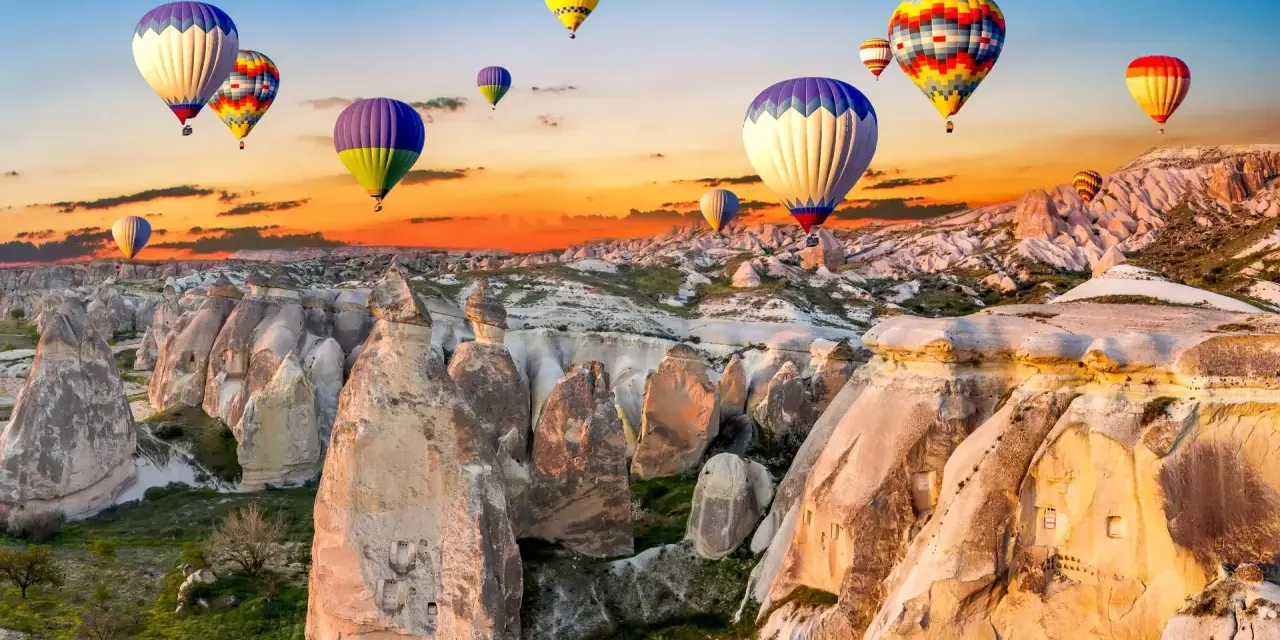 Kolorowe balony unoszą się nad skalistym krajobrazem Kapadocji o wschodzie słońca. Idealne miejsce na wakacje all inclusive!