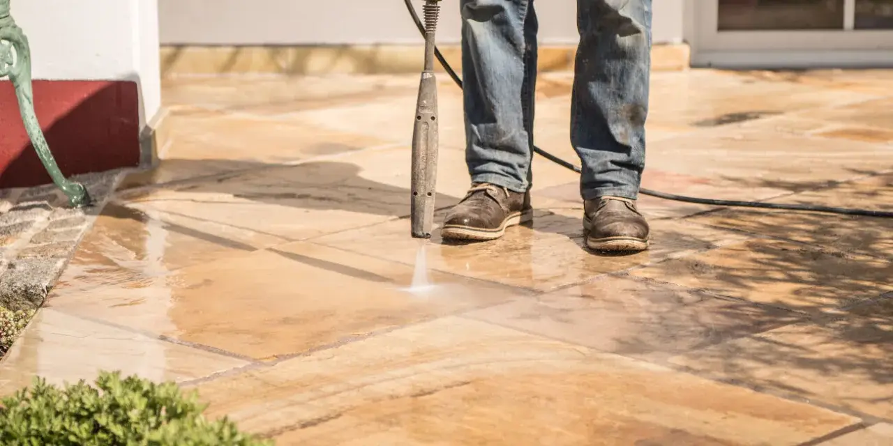 Nettoyer carrelage extérieur noirci avec un nettoyeur haute pression. L'eau projetée révèle la beauté naturelle des dalles.