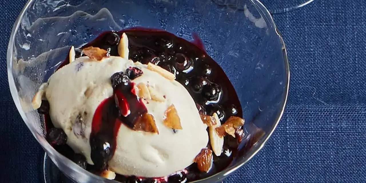 Cremiges Malaga Eis Rezept mit Blaubeersauce und Mandelsplittern in einer Glasschale.