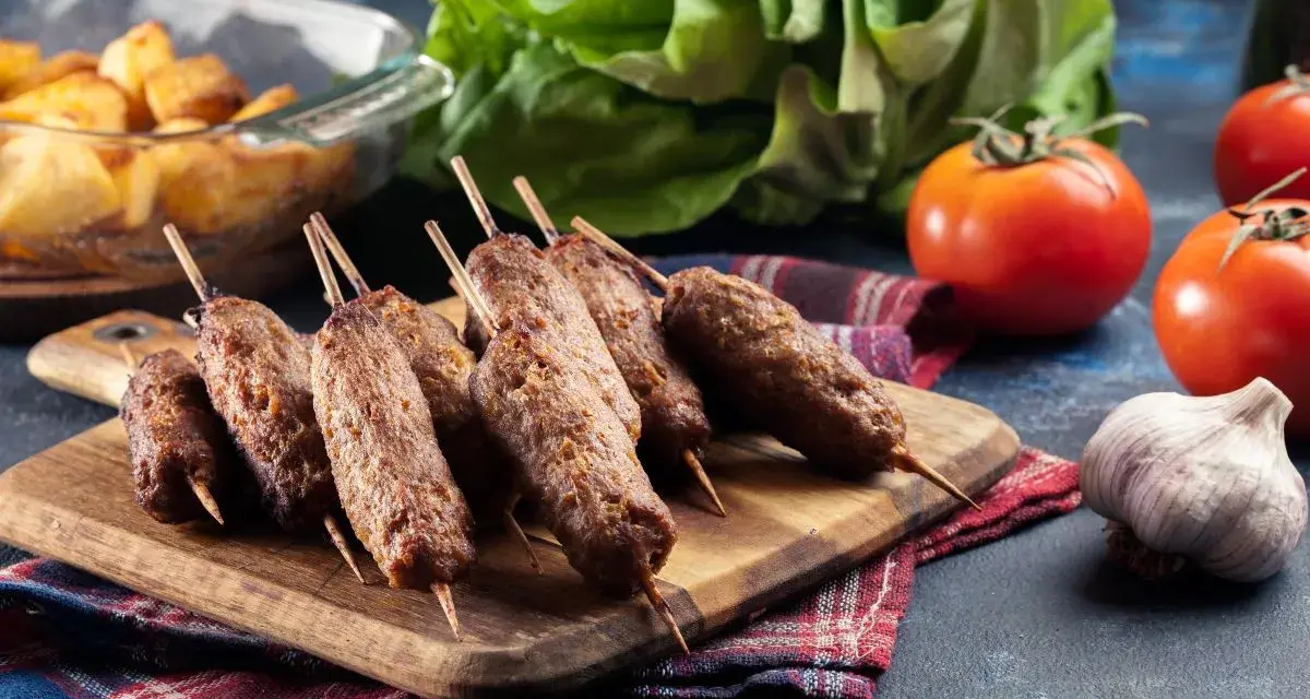 Aksamitne ćevapi na drewnianej desce, obok pomidory, czosnek i pieczone ziemniaki. Pyszny posiłek gotowy do podania.