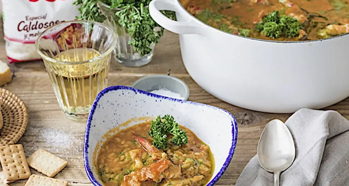 Delicioso arroz con bogavante servido en un cuenco, con una cazuela llena y una bolsa de arroz SOS al fondo.