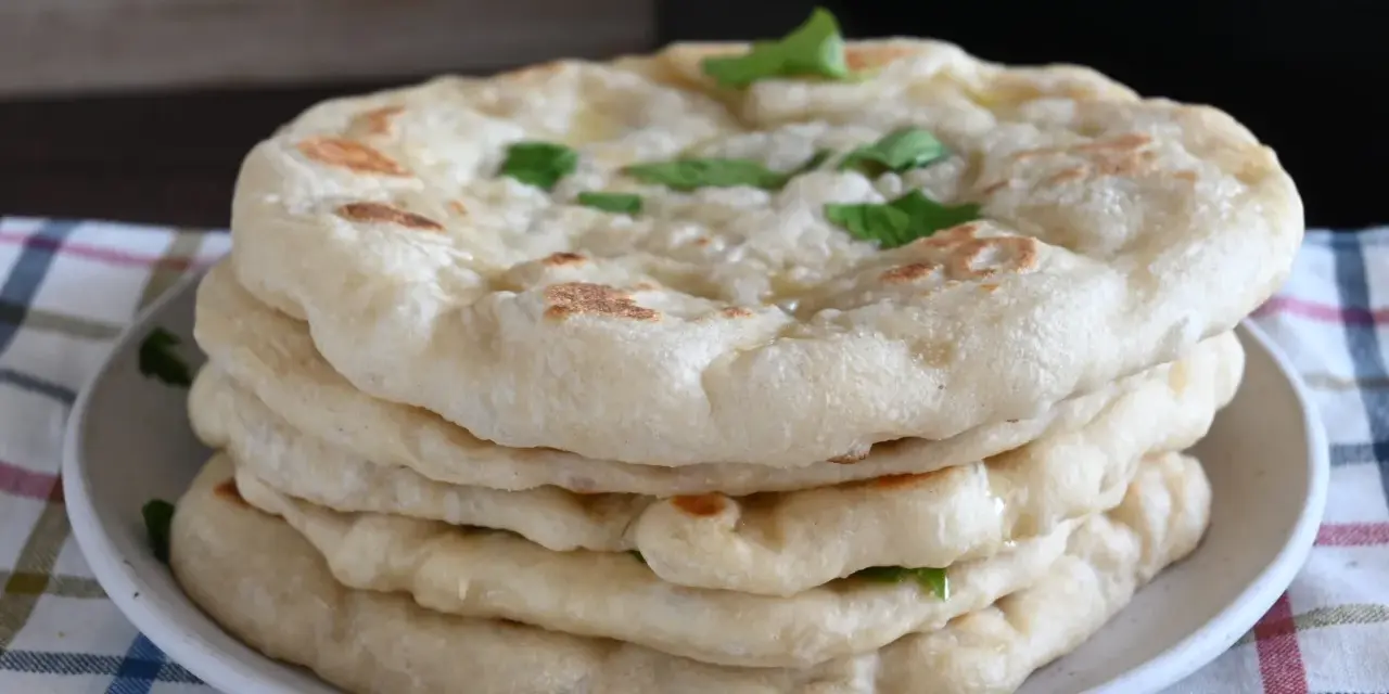 Pila di pane in padella, soffice e dorato, guarnito con erbe fresche. Perfetto per accompagnare ogni pasto.