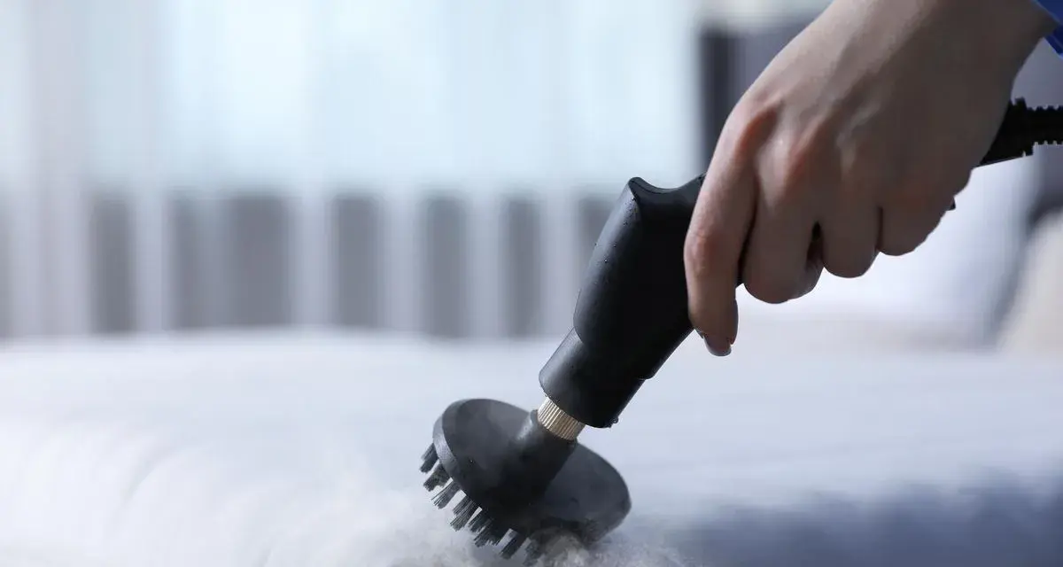 Main d'une personne utilisant un nettoyeur vapeur pour nettoyer un matelas en mousse. Une méthode efficace pour savoir comment nettoyer un matelas en mousse.