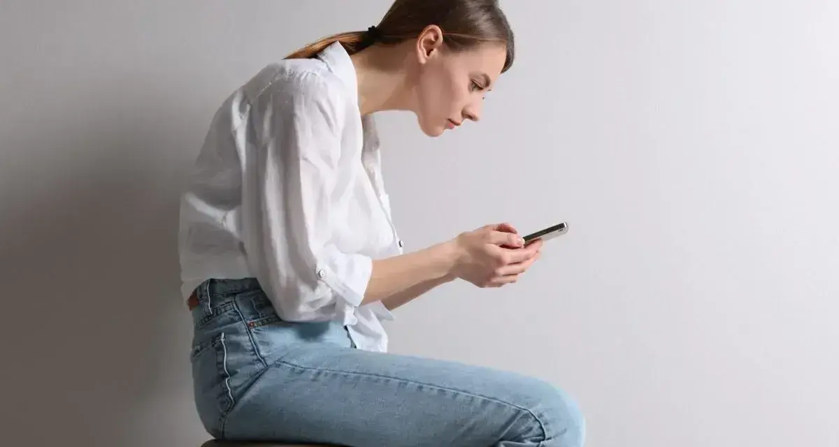 Frau mit gebeugtem Rücken und Handy. Schlechte Haltung kann zu einem Buckel im Nacken Ursache sein.