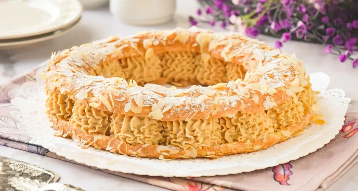 Un delicioso praliné que es un pastel Paris-Brest, cubierto de almendras laminadas y espolvoreado con azúcar glas.