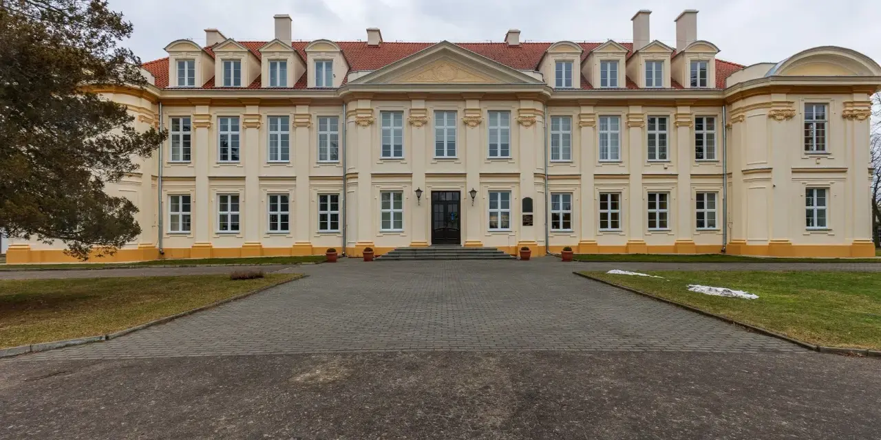 Pałac biskupów kujawskich w Wolborzu, okazała budowla z żółtą fasadą i czerwonym dachem, otoczona zielenią i brukowanym podjazdem.