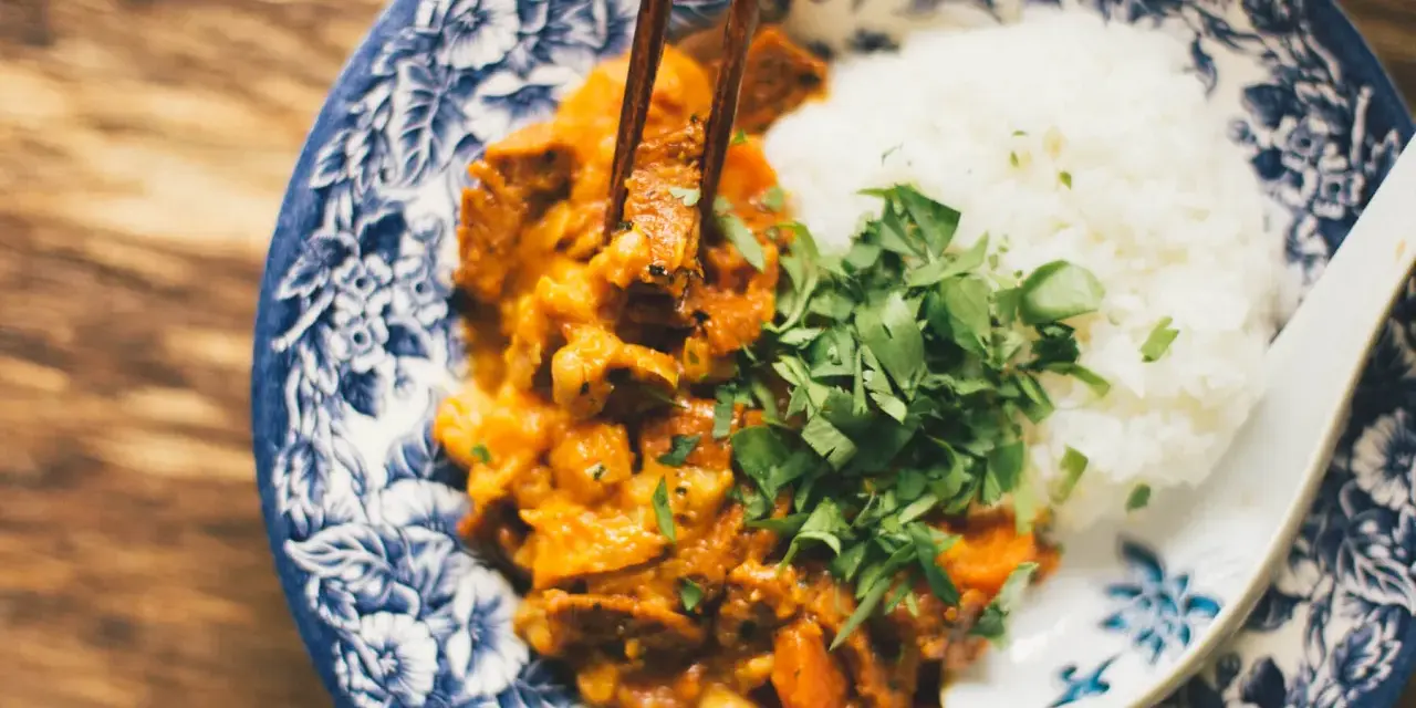Miseczka z ryżem i curry, podana z posiekaną natką pietruszki, jedzona pałeczkami.