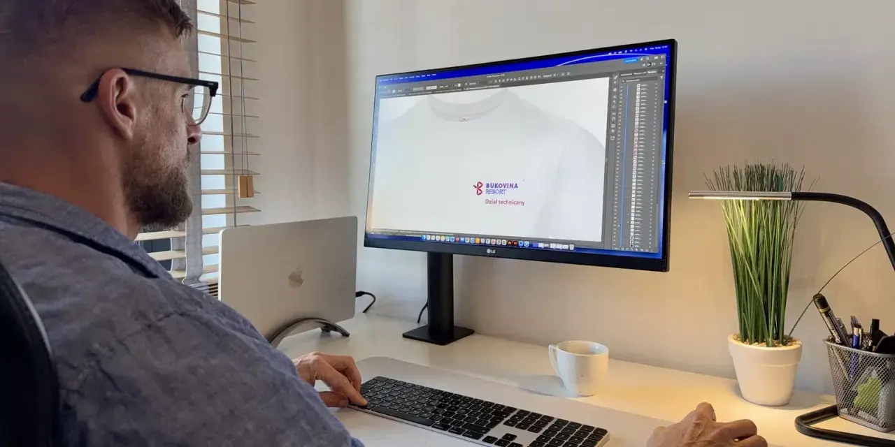Mężczyzna pracuje przy komputerze, projektując logo na koszulkę. Pokazuje, jak napisać tekst na komputerze i go wydrukować.