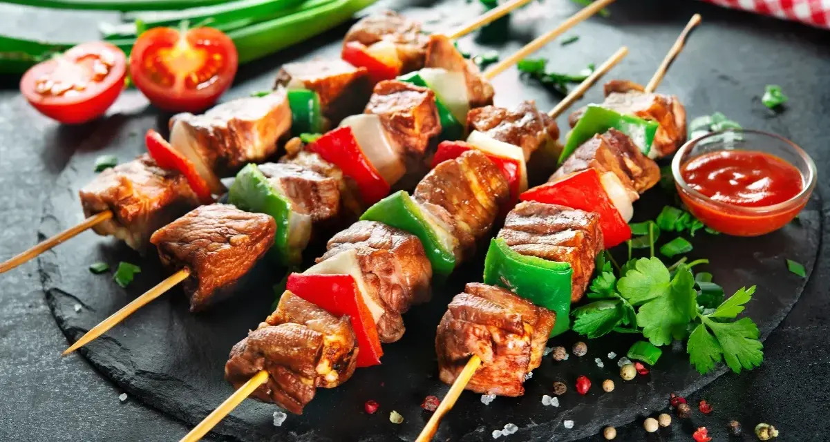 Spiedini di carne succulenti con peperoni e cipolle, pronti per essere gustati con una salsa rossa e pomodorini freschi.