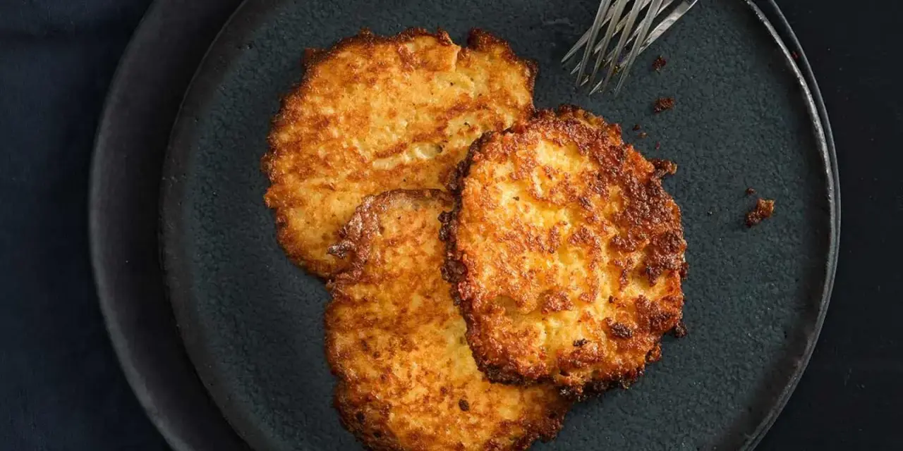 Drei goldbraune Kartoffelpuffer, frisch zubereitet im Thermomix, liegen auf einem dunklen Teller.
