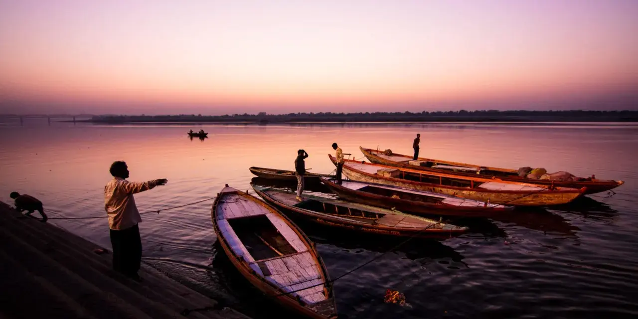 Vue d'ensemble de bateaux amarrés sur un fleuve au crépuscule, avec des silhouettes humaines sur la rive. Ces photos grand angle capturent la sérénité du moment.