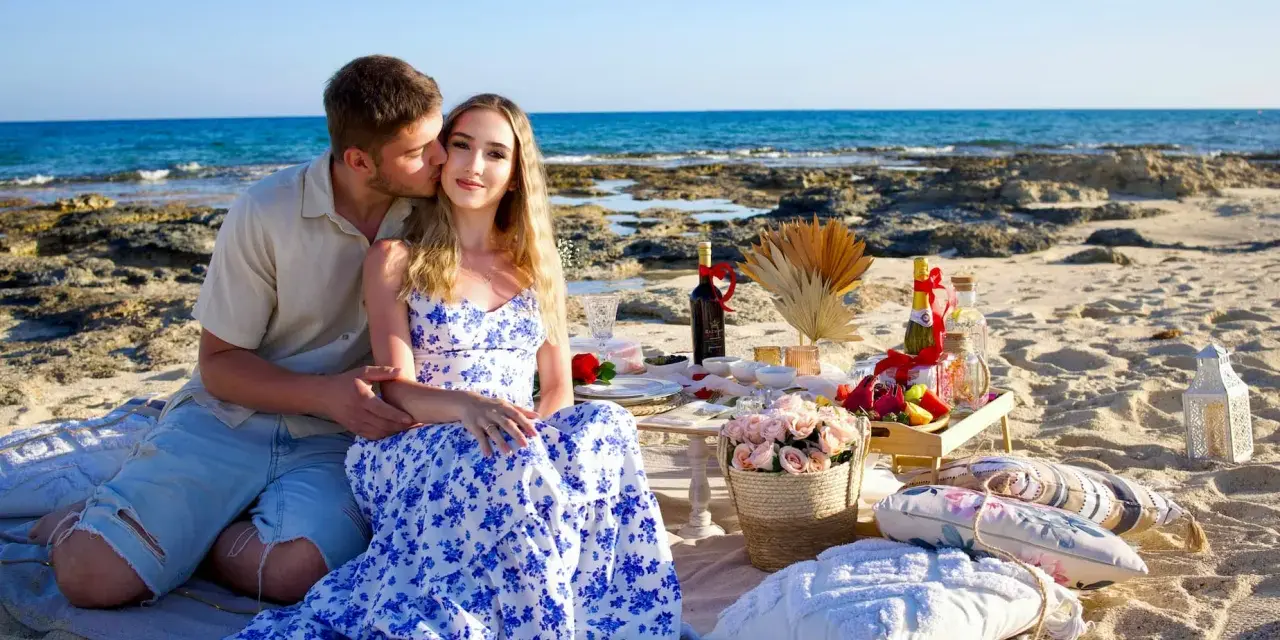Romantyczny piknik na plaży podczas wakacji na Cyprze. Para cieszy się chwilą przy winie i owocach, z widokiem na morze.
