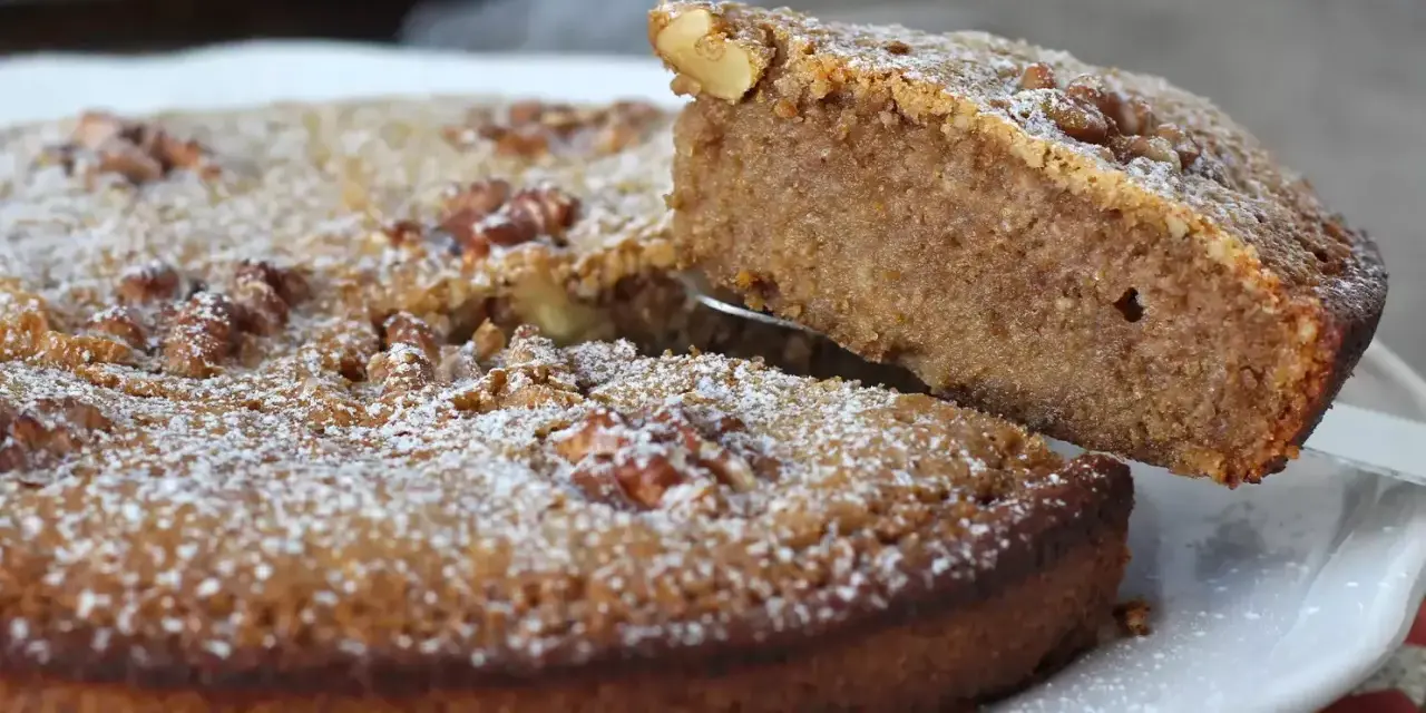 Une part est soulevée d'un délicieux gâteau aux noix, saupoudré de sucre glace.
