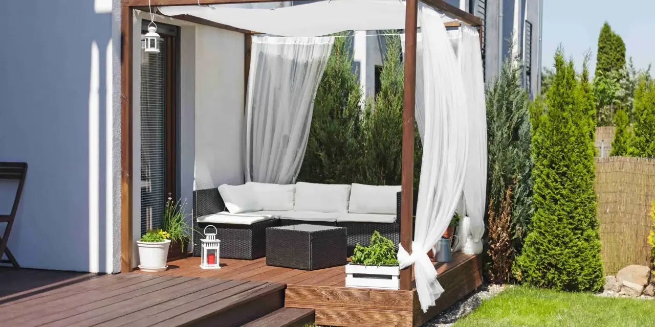 Drewniana pergola z białymi zasłonami to idealne miejsce na tarasie. Zasłony powieszone na drewnianej konstrukcji tworzą przytulną atmosferę.