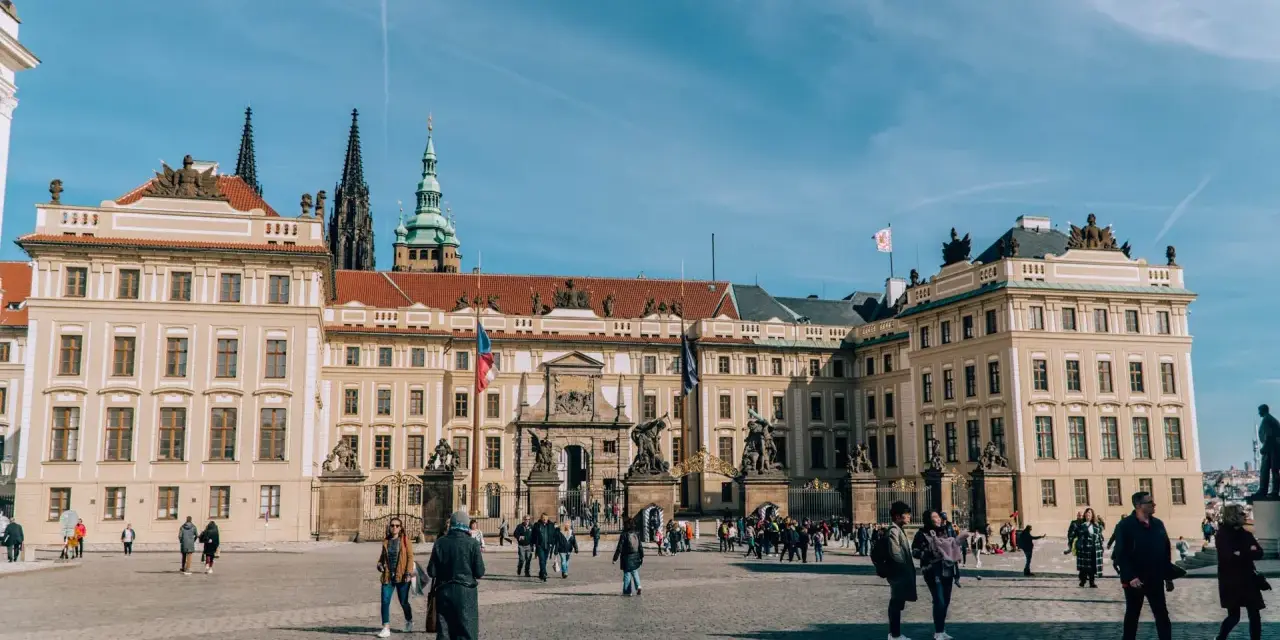 Tłum turystów spaceruje po dziedzińcu przed imponującym zamkiem na Hradczanach.