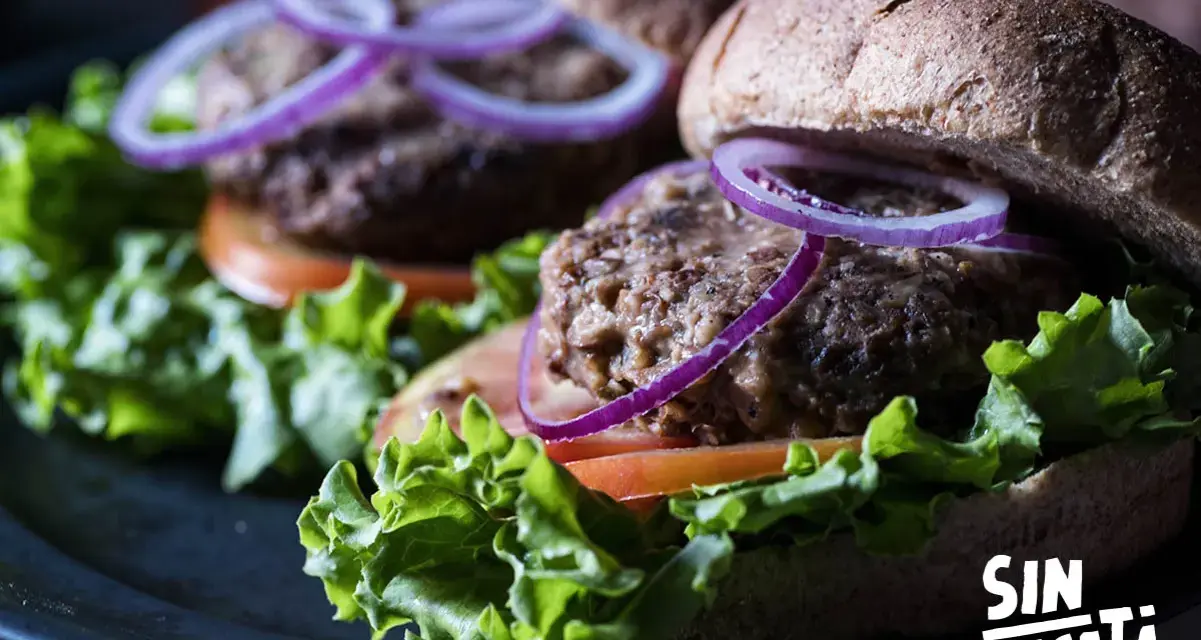 Dos deliciosas hamburguesas de lentejas con lechuga fresca, tomate y aros de cebolla morada, listas para disfrutar.