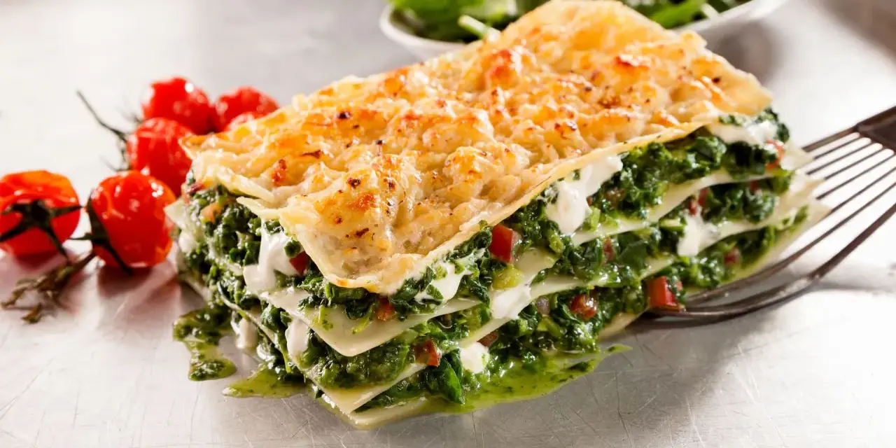 Deliciosa lasaña de verduras, con capas de pasta, espinacas y queso cremoso, acompañada de tomates cherry.