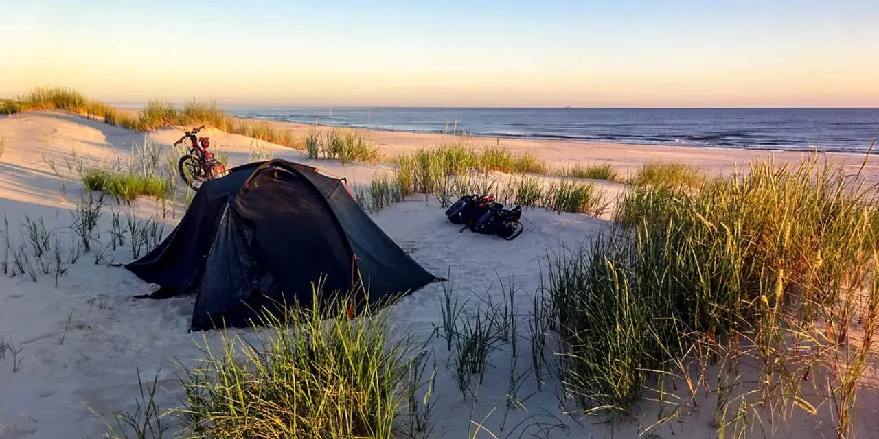 Namiot i rower na plaży, idealne miejsce na biwakowanie na dziko. Wschód słońca nad morzem.