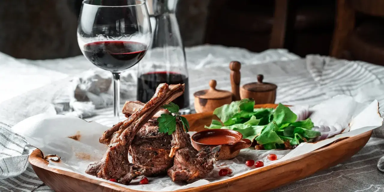 Saftige Lammkoteletts mit frischem Salat und einem Glas Rotwein. Die perfekte Wahl, welcher Wein zu Lamm passt, ist oft ein kräftiger Rotwein.