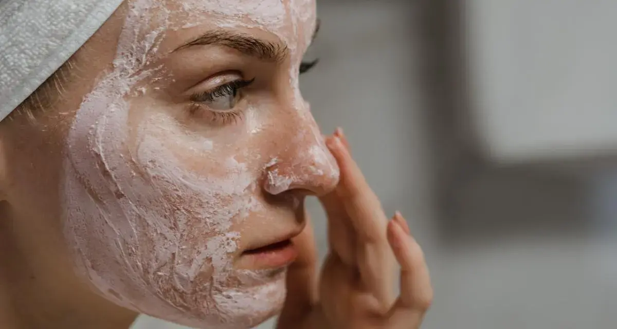 Mujer con mascarilla rosa en la cara, aprendiendo como exfoliar la cara para una piel radiante.