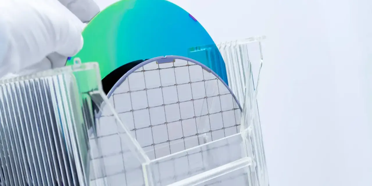 A gloved hand holds a silicon wafer, its grid pattern visible. Another wafer, iridescent blue and green, rests behind it. This image explores the question: is plastic a semiconductor?