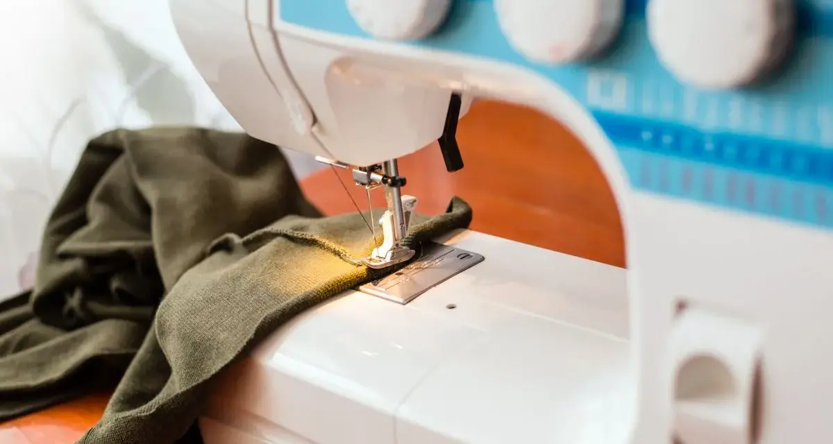 Maszyna do szycia z zieloną tkaniną. Zastanawiasz się, dlaczego maszyna do szycia zrywa górną nitkę? Może problem tkwi w igle lub naprężeniu?