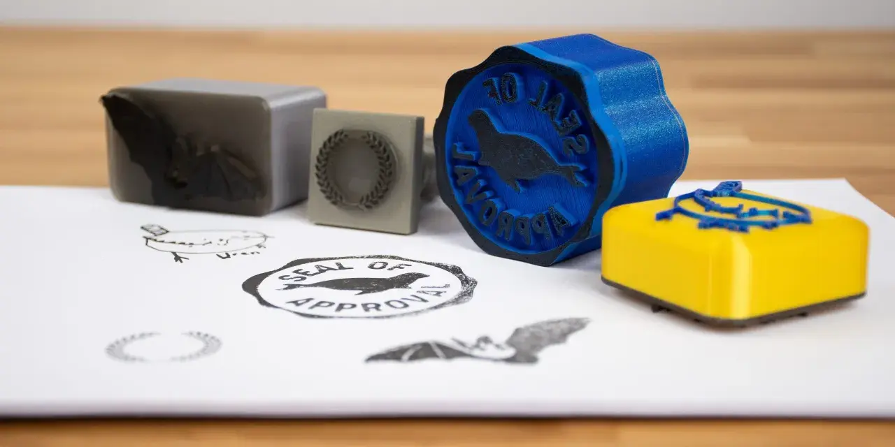 A blue 3d print stamp with a seal of approval design sits next to a yellow one.