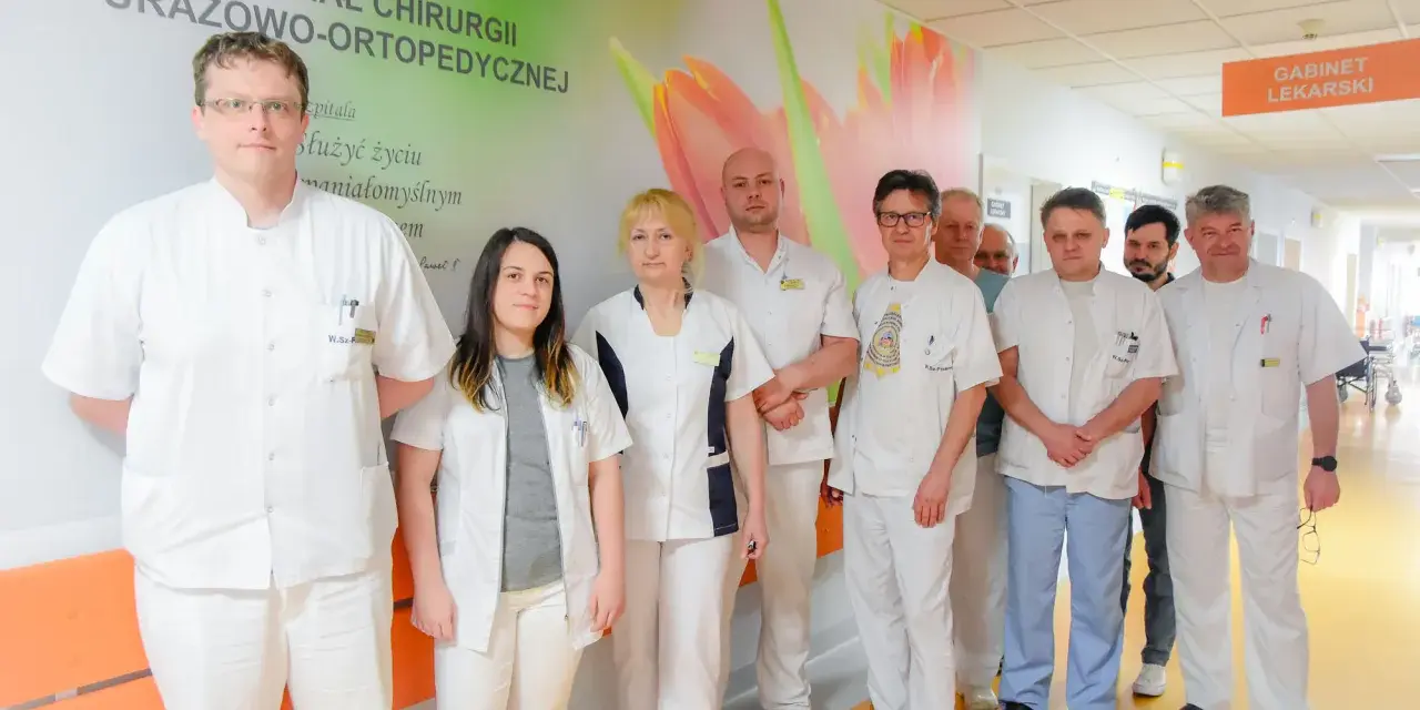 Grupa lekarzy w białych fartuchach stoi w szpitalnym korytarzu.