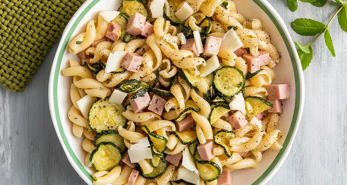 Un'insalata di pasta fredda sfiziosa con fusilli, zucchine grigliate, cubetti di prosciutto cotto e scaglie di formaggio.