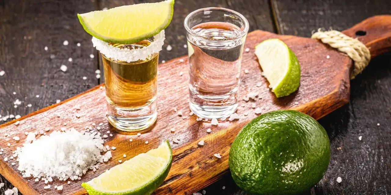 Zwei Gläser Tequila, Salz und Limettenspalten auf einem Holzbrett. Perfekt zum Tequila trinken.