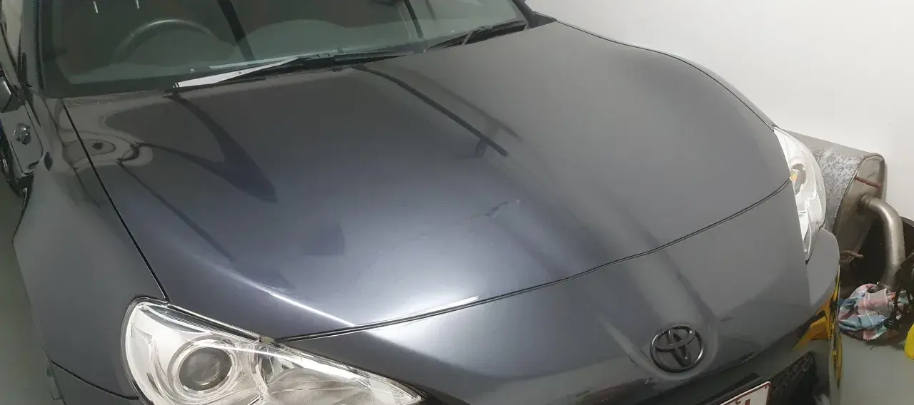 A dark grey car hood with a Toyota emblem. The paint has some minor imperfections, hinting at the question: how long does it take to clay bar a car?